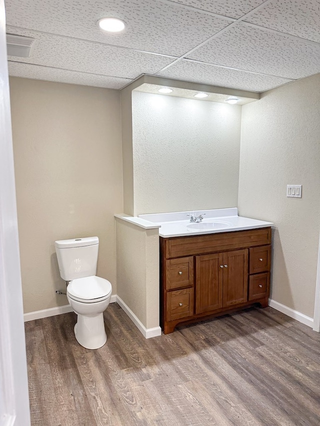 bathroom with vanity, wood-type flooring, a paneled ceiling, and toilet