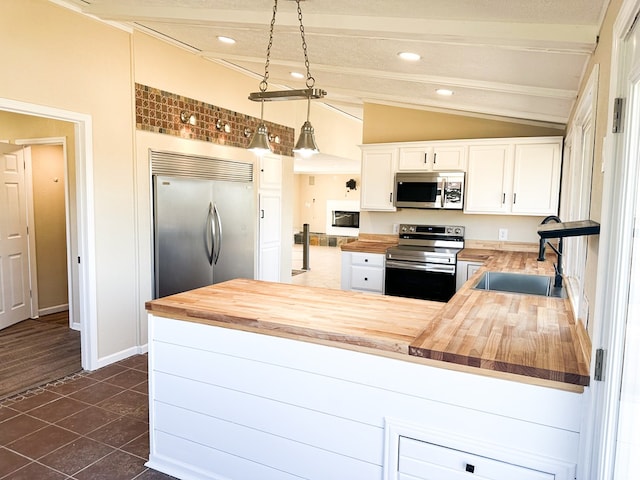 kitchen featuring wood counters, kitchen peninsula, stainless steel appliances, white cabinets, and hanging light fixtures