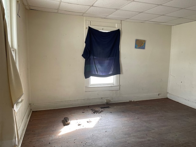 spare room with baseboards, a drop ceiling, and wood finished floors