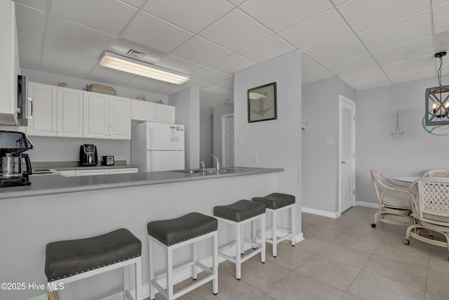 kitchen featuring a sink, white cabinets, freestanding refrigerator, a peninsula, and a drop ceiling