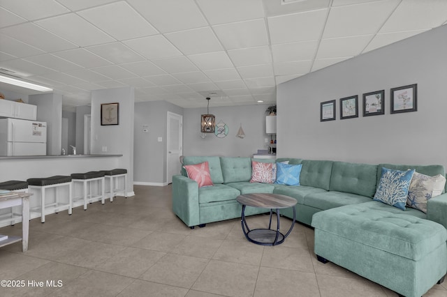 living area featuring light tile patterned floors, an inviting chandelier, and a paneled ceiling