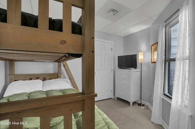 bedroom with visible vents, a heating unit, baseboards, a drop ceiling, and light tile patterned floors