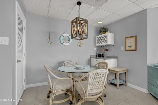 dining room featuring light tile patterned floors, baseboards, a paneled ceiling, and a notable chandelier
