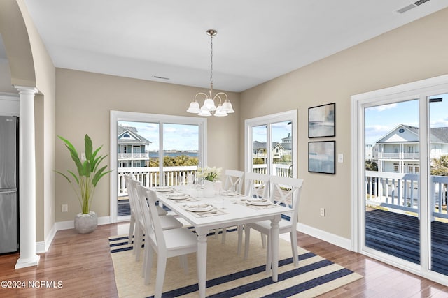 dining space with wood-type flooring, a chandelier, and decorative columns