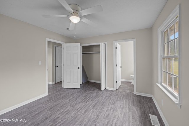 unfurnished bedroom featuring dark hardwood / wood-style floors, ensuite bath, ceiling fan, and multiple windows