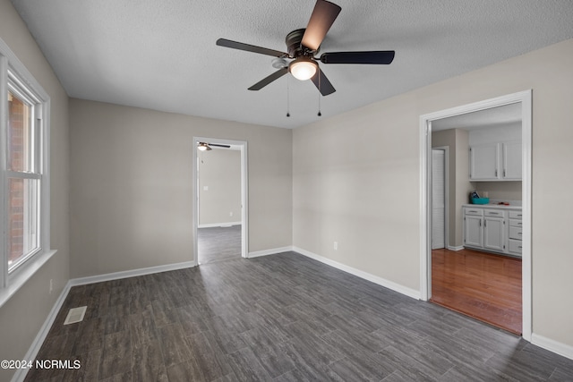 unfurnished room featuring a textured ceiling, ceiling fan, a wealth of natural light, and dark wood-type flooring