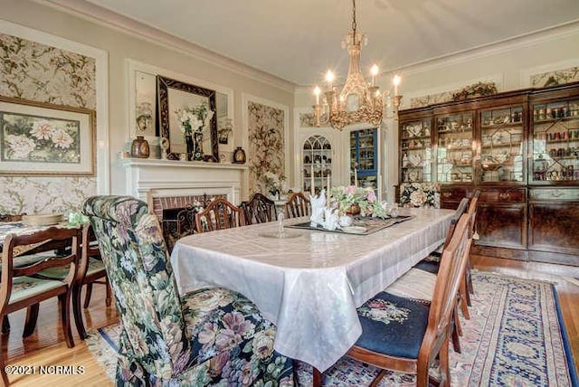 dining space featuring crown molding, a brick fireplace, a notable chandelier, and light wood-type flooring