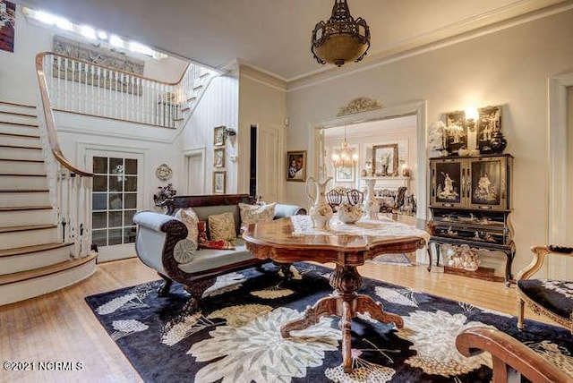 sitting room with an inviting chandelier, light hardwood / wood-style floors, a towering ceiling, and ornamental molding