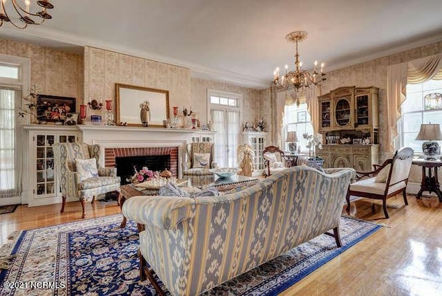living room with light hardwood / wood-style flooring, ornamental molding, a brick fireplace, and a notable chandelier