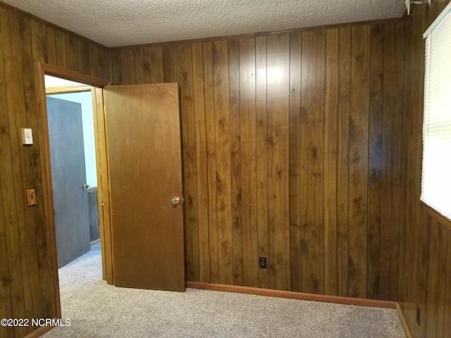 carpeted empty room with wood walls and a textured ceiling