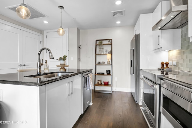 kitchen featuring dark wood-style flooring, wall chimney exhaust hood, white cabinets, a sink, and appliances with stainless steel finishes