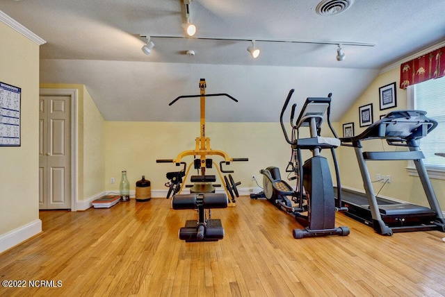 exercise room featuring rail lighting, light hardwood / wood-style floors, and a textured ceiling