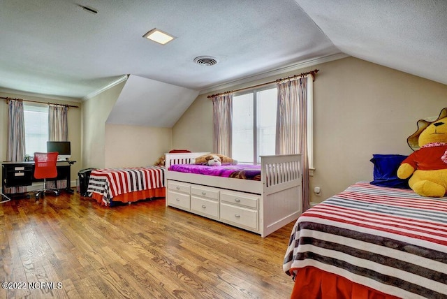 bedroom featuring multiple windows, vaulted ceiling, light hardwood / wood-style flooring, and a textured ceiling