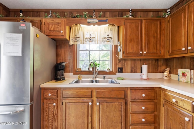 kitchen featuring wood walls, stainless steel refrigerator, a textured ceiling, and sink