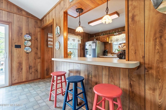 kitchen featuring stainless steel fridge, pendant lighting, wood walls, and a kitchen breakfast bar