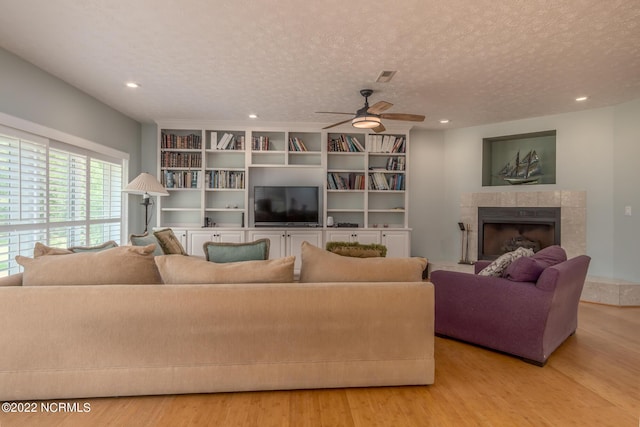 living room featuring ceiling fan, a tile fireplace, light hardwood / wood-style floors, and a textured ceiling