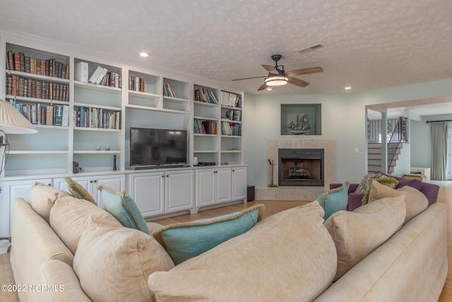 living room with a tile fireplace, ceiling fan, a textured ceiling, light hardwood / wood-style flooring, and built in shelves