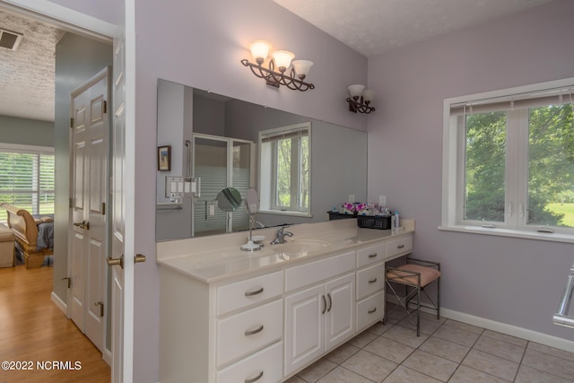 bathroom with a notable chandelier, vanity, a textured ceiling, and a healthy amount of sunlight