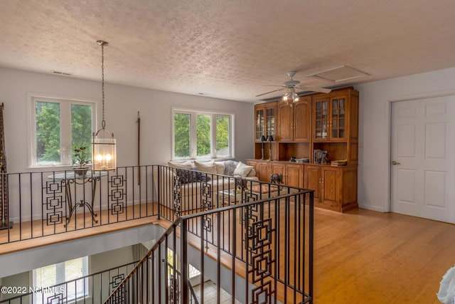 hall with light hardwood / wood-style flooring, a textured ceiling, and an inviting chandelier