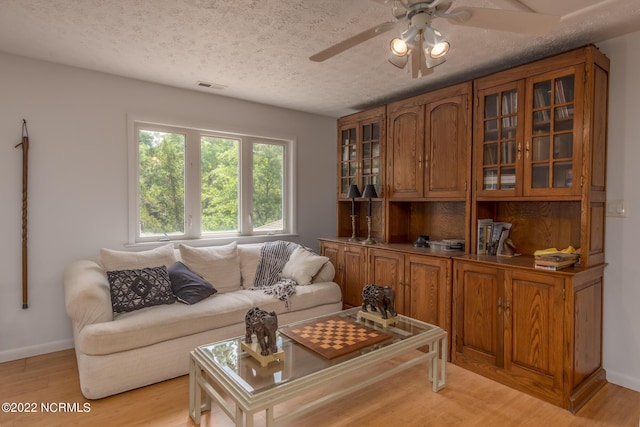 living room with a textured ceiling, ceiling fan, and light hardwood / wood-style flooring