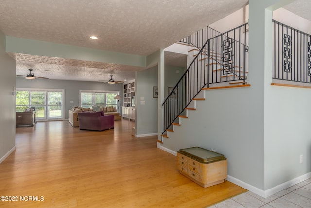 stairway with a textured ceiling, ceiling fan, and light wood-type flooring