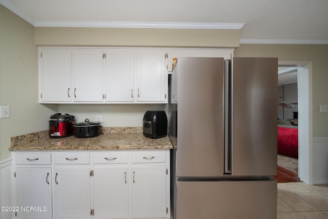 kitchen featuring light stone countertops, stainless steel refrigerator, and white cabinetry