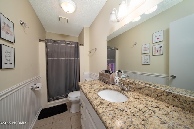 bathroom with tile flooring, a textured ceiling, vanity with extensive cabinet space, and toilet