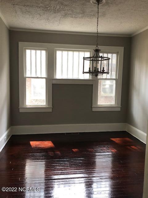 unfurnished dining area with a notable chandelier, a textured ceiling, dark wood-type flooring, and crown molding