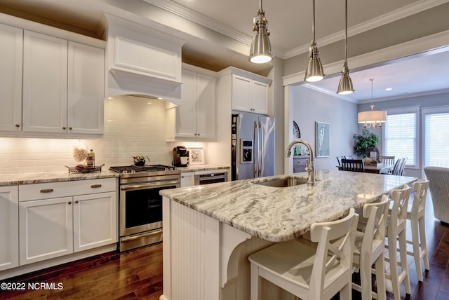 kitchen featuring appliances with stainless steel finishes, white cabinets, a center island with sink, pendant lighting, and sink