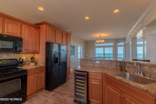 kitchen with a chandelier, light hardwood / wood-style floors, wine cooler, black appliances, and sink