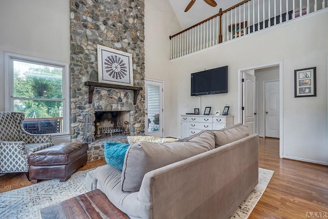 living room with ceiling fan, light wood-type flooring, high vaulted ceiling, and a stone fireplace