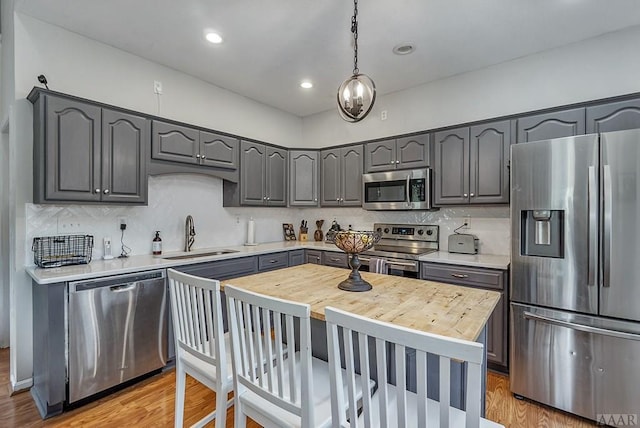 kitchen with appliances with stainless steel finishes, light wood-type flooring, a center island, backsplash, and sink