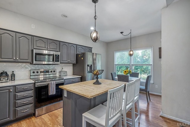 kitchen with stainless steel appliances, a kitchen island, decorative light fixtures, backsplash, and light wood-type flooring