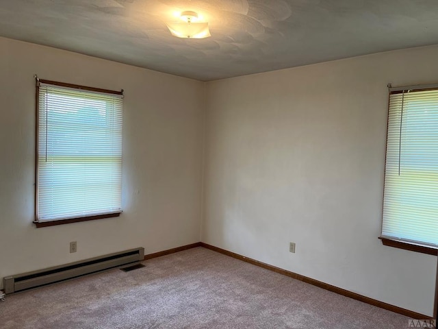 empty room with carpet flooring, a wealth of natural light, and a baseboard heating unit