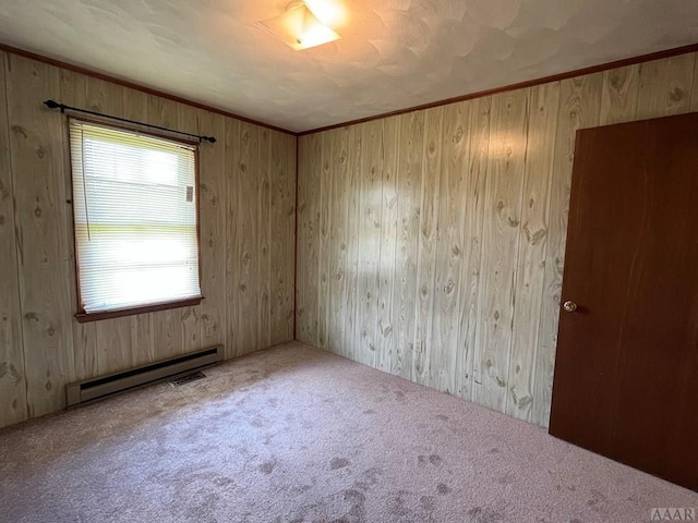 unfurnished room featuring wooden walls, carpet flooring, a baseboard heating unit, and crown molding