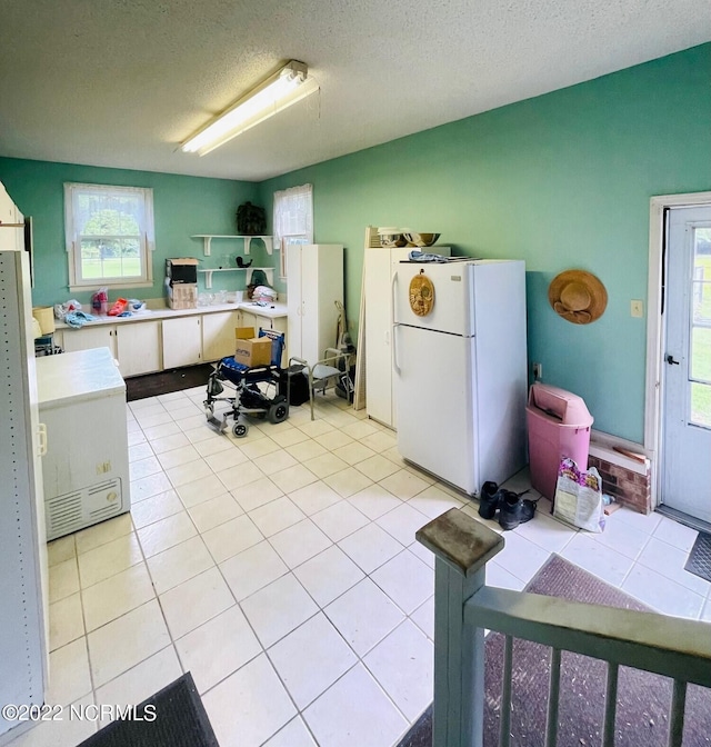 kitchen with plenty of natural light, a textured ceiling, light tile flooring, and white refrigerator