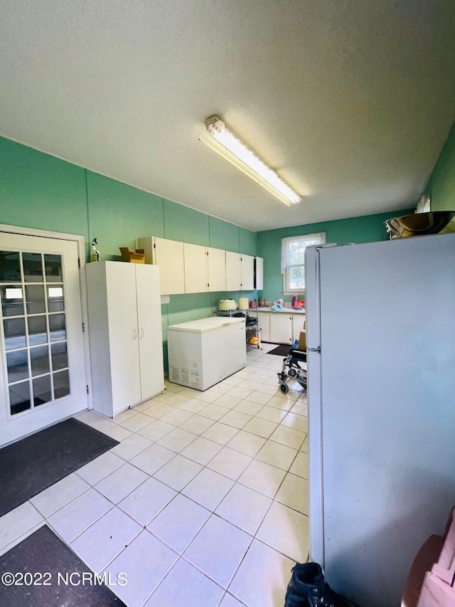 kitchen featuring white cabinets, light tile floors, white fridge, and a textured ceiling