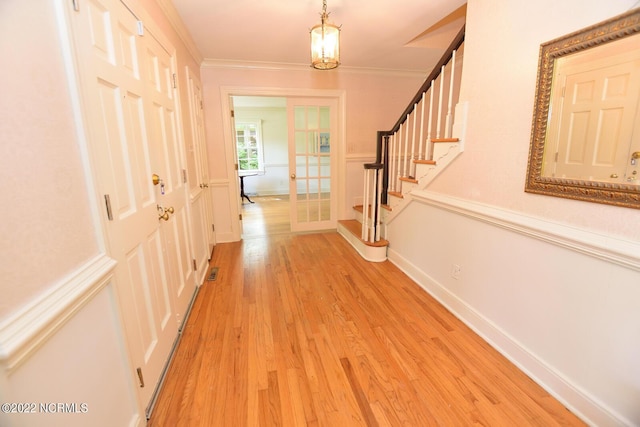 hallway with a chandelier, light hardwood / wood-style floors, french doors, and ornamental molding