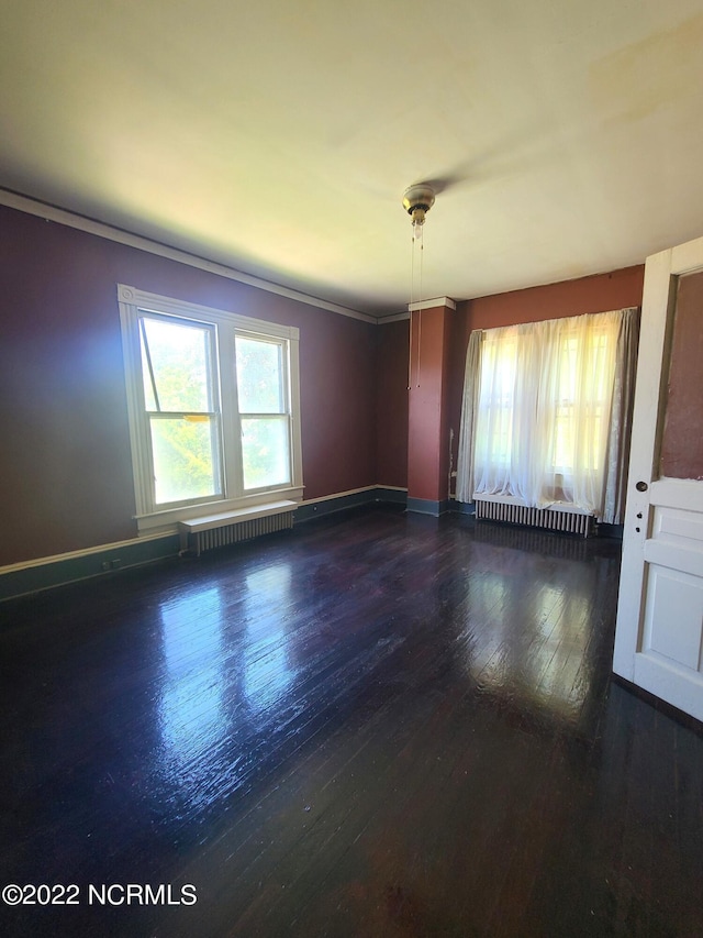 empty room with crown molding, dark hardwood / wood-style flooring, and radiator