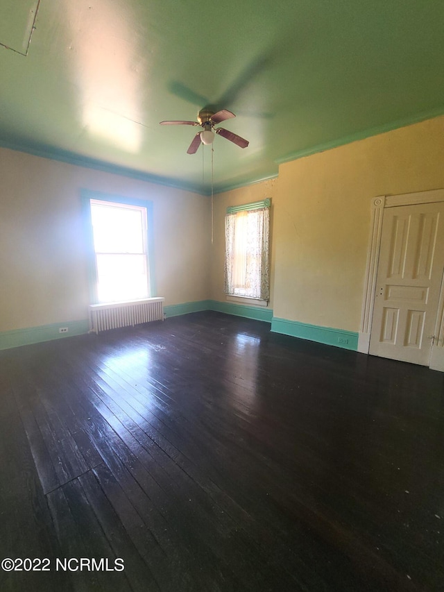 empty room featuring dark hardwood / wood-style floors, ceiling fan, and radiator heating unit