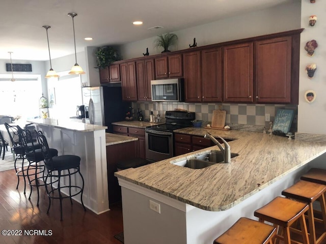 kitchen featuring dark hardwood / wood-style floors, appliances with stainless steel finishes, a breakfast bar area, tasteful backsplash, and decorative light fixtures