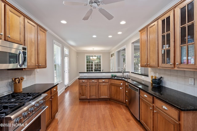 kitchen with kitchen peninsula, crown molding, stainless steel appliances, ceiling fan with notable chandelier, and light wood-type flooring