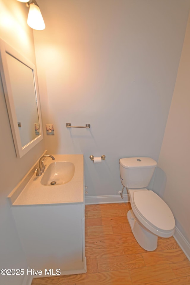 half bathroom with baseboards, toilet, wood finished floors, and vanity