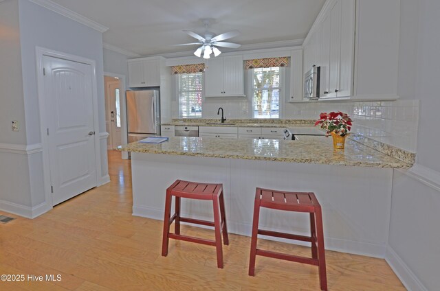 kitchen featuring white cabinetry, kitchen peninsula, crown molding, appliances with stainless steel finishes, and light wood-type flooring