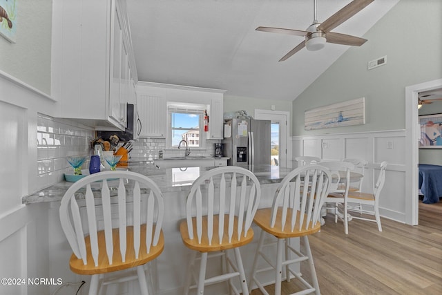 kitchen featuring lofted ceiling, white cabinets, tasteful backsplash, light hardwood / wood-style floors, and stainless steel appliances