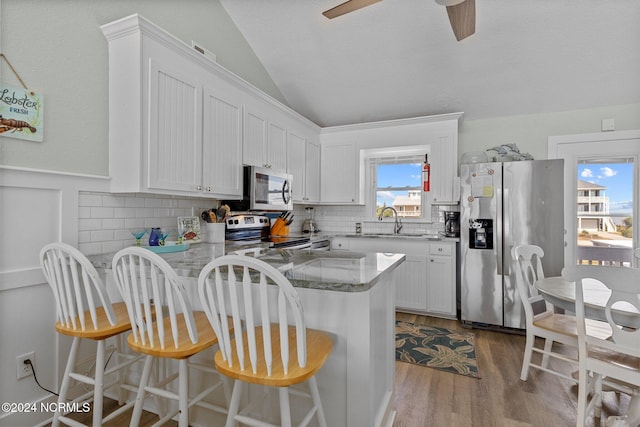 kitchen with lofted ceiling, light hardwood / wood-style flooring, kitchen peninsula, stainless steel appliances, and white cabinetry