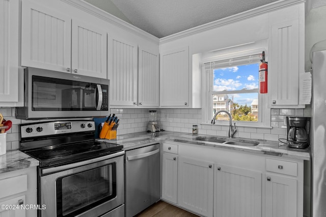 kitchen with light stone counters, appliances with stainless steel finishes, a textured ceiling, white cabinetry, and sink