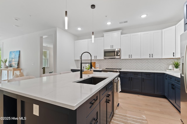 kitchen featuring sink, white cabinetry, decorative light fixtures, stainless steel appliances, and a kitchen island with sink