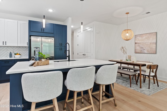 kitchen featuring sink, a center island with sink, light wood-type flooring, stainless steel fridge, and pendant lighting