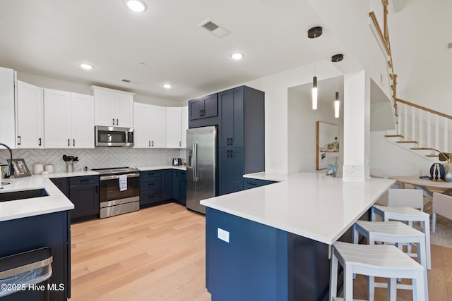 kitchen featuring white cabinetry, a breakfast bar area, hanging light fixtures, kitchen peninsula, and stainless steel appliances